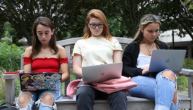 Three girls on a bench using their laptop computers.