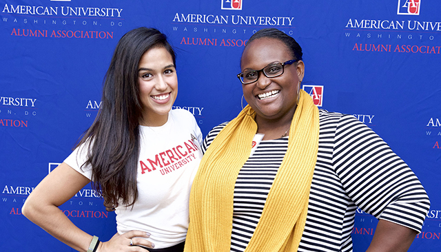 Two alumni volunteers in front of step and repeat banner