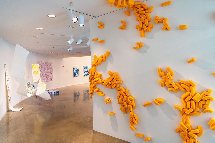 AU MFA Studio Art thesis exhibition: paper or textile draped from ceiling and curved orange sculpture arrangement installed on wall