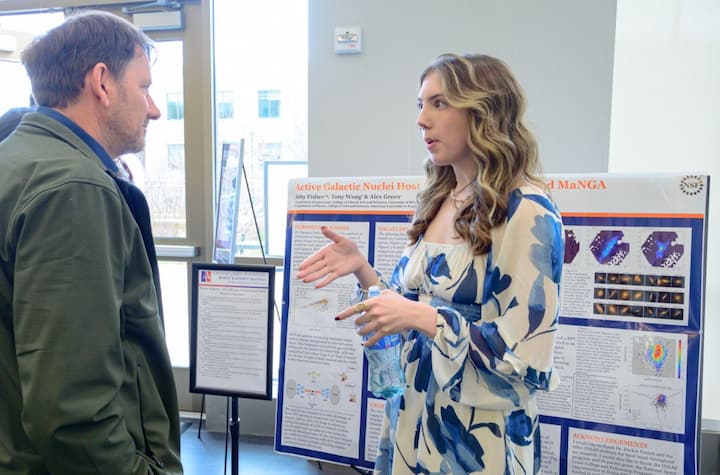 Physics student discussing poster with faculty.