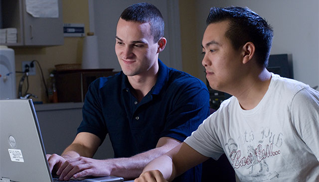 Two male students work on a laptop together.