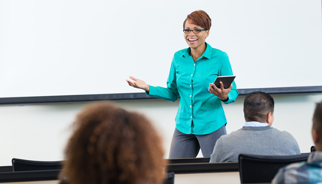 Female faculty at front of class with three students in the foreground