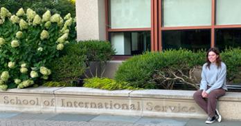 Ainsley Ghaman sits on the edge of the concrete sign for School of International Service