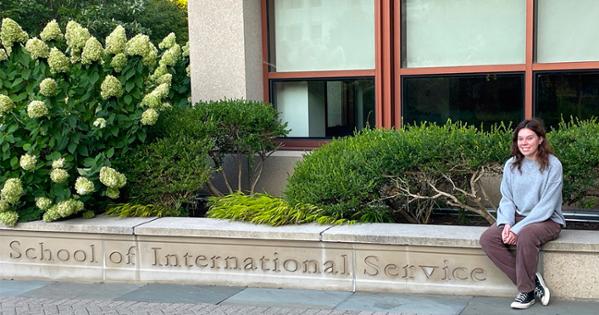 Ainsley Ghaman sits on the edge of the concrete sign for School of International Service