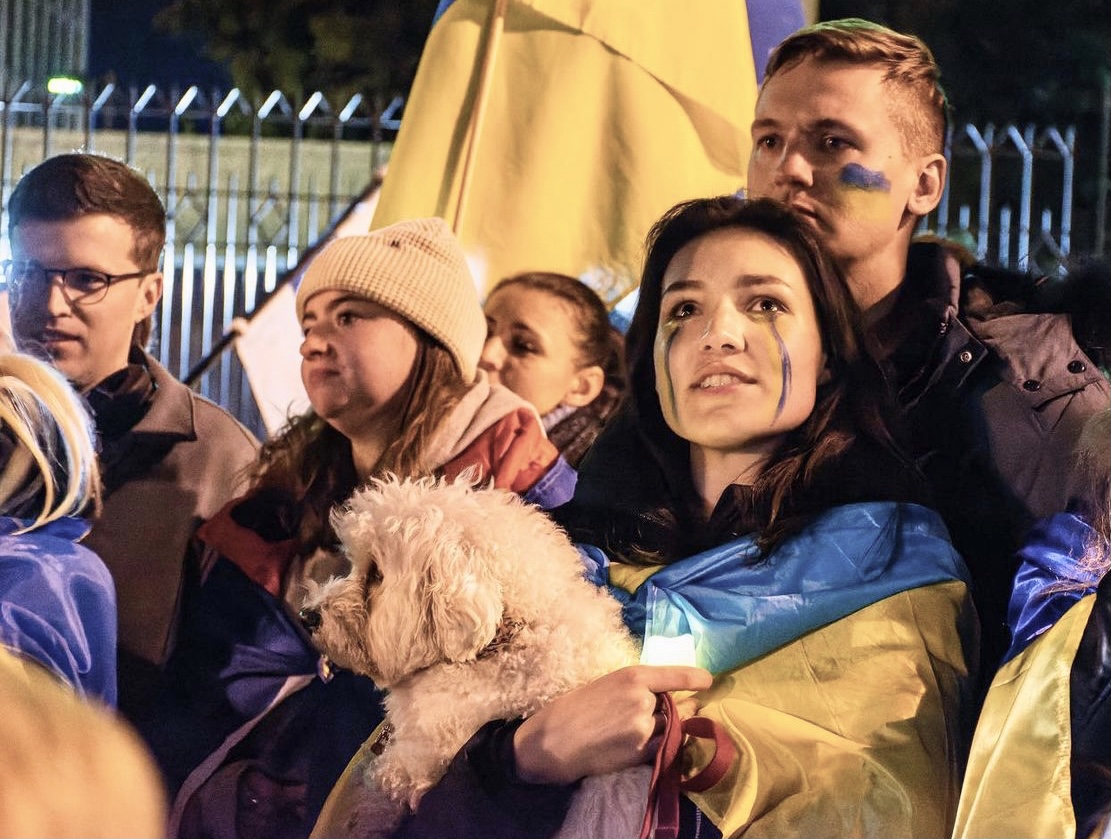 Anastasiia Baydyuk wears a Ukrainian flag and holds a dog during a gathering of students 