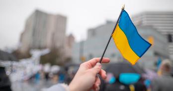 Child's hand waving small Ukrainian flag with city building in background