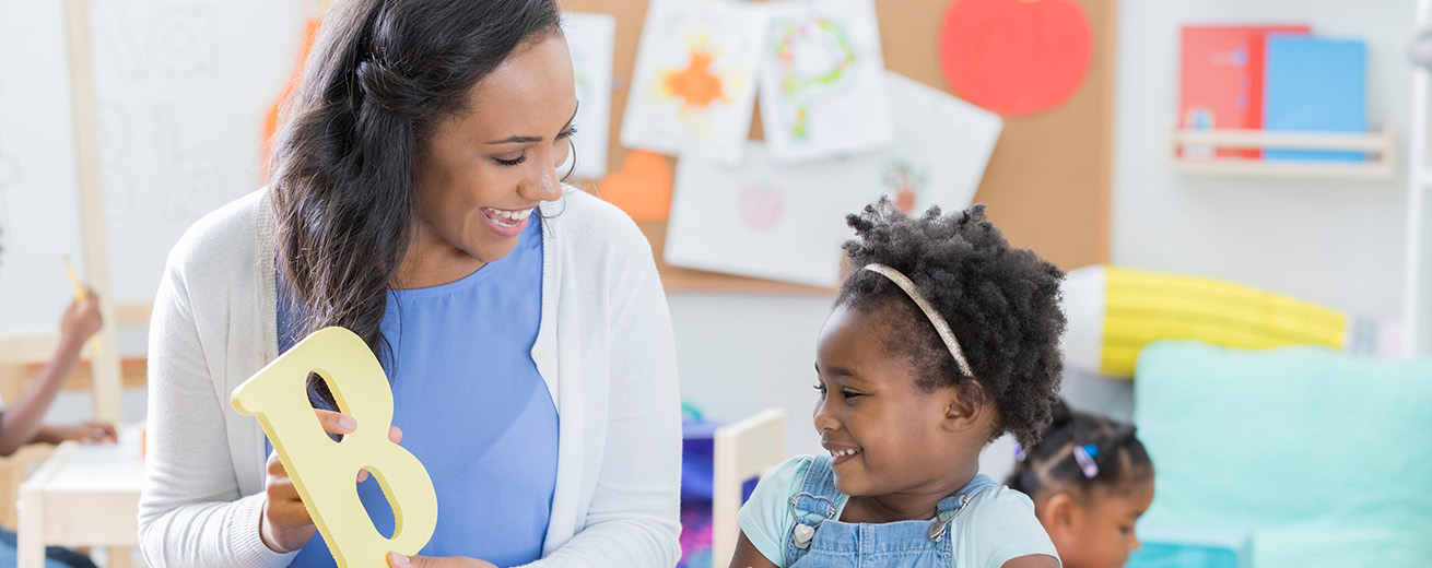 Teacher holding up a wooden "B" to teach a young student.