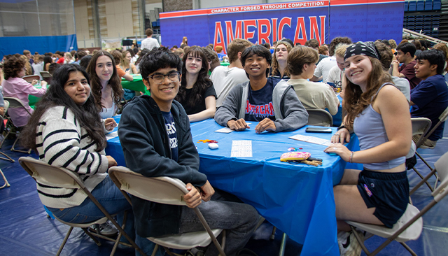 Students smile at the camera from a table set up in Bender Arena.